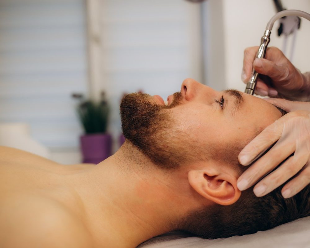 A cosmetologist is making the procedure Microdermabrasion of the facial skin in a beauty salon. Cosmetology for men and professional skin care. High quality photo SSUCv3H4sIAAAAAAAAA41PQY6DMAz8i88gNSQClq9UewiJ21oFUiWm1Qrl7+tQqr1uTjOeeGa8AXkYQHdt22lzqr+MUrVSiLV1xtTNpWu8Nlbp5gIVeMsIg9LatLrpe9U0fXeSV8FoEzkYNqBpWhNHyxQWGESJuHiMO0RPHCLZSViuILHlNWGSNWFOvK+i7vzjd97KXApKeFrHAnL1z9l3BfaKi/sp/rkUmdDucWeR7i/GOB/ZgW+lYoGPSI6W69FJTgnzGy+By+6ewMHdyR/L7zNuJNNYsmB9TMF69Ie8jjMxf2jEJ+Hr73fO+RcNh2D6hAEAAA==
